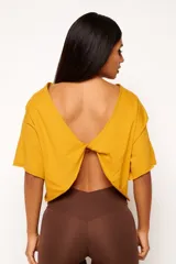 Remera color mostaza de corte holgado, con mangas cortas y espalda abierta con detalle de nudo. Confeccionada en algodón sustentable.