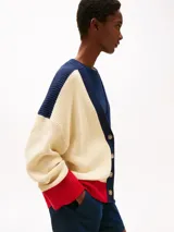 Cárdigan de punto color crema, con cuello en V, cierre con botones y corte amplio. Presenta detalles en azul marino en los hombros y en el borde del cuello, y detalles en rojo en los puños y en el ruedo. Logo de Tommy Hilfiger bordado en el pecho.