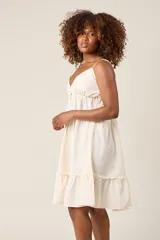 Vestido corto lila con breteles finos, escote en V con botones y falda escalonada con volados.