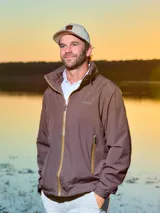 Campera marrón de poliéster, impermeable y liviana, con cierre frontal y bolsillos laterales con cierre. Tiene cuello alto con capucha oculta y logo de la marca bordado en el pecho.