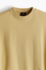 Remera color mostaza de algodón de peso medio, corte oversized, con cuello redondo ribeteado, hombros caídos y bajo recto.