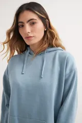 Buzo hoodie lila con capucha y cordones ajustables, bolsillo tipo canguro y corte holgado.