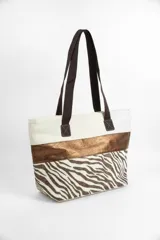 Bolso tipo tote bag de tela color beige con estampado de estrellas negras en la parte inferior y una franja horizontal negra brillante en el medio. Tiene asas de tela color beige claro y detalles de cuero sintético negro en los puntos de unión de las asas.