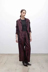 Pantalón de tafeta tornasolada color borgoña, de corte recto con cintura elastizada, bolsillos frontales con cierre plateado, y cordones ajustables en las pantorrillas para fruncir el bajo.