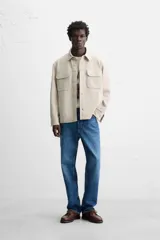 Sobrecamisa color beige de corte relaxed fit, con cuello solapa, manga larga con puños abotonados, bolsillos de plastrón con solapa en el pecho y bolsillos de vivo en la cadera. Cierre frontal con botones.