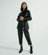 Chaqueta larga de cuero sintético negro, con cuello camisero, cierre frontal con botones, cinturón con hebilla, bolsillos con solapa y puños abotonados.