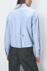 Camisa celeste de algodón con corte crop, cuello solapa, mangas largas con puños y cierre frontal con botones ocultos.