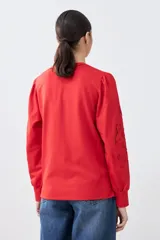 Sweatshirt rojo de manga larga con cuello redondo y calados bordados en los hombros y mangas.