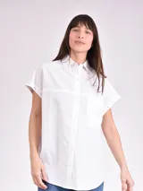 Camisa celeste de corte amplio, con cuello clásico, cierre frontal con botones, bolsillo en el pecho y mangas largas con detalle de botones en los puños.