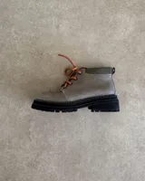 Borcego color gris con cordones color naranja, suela track color negro y detalle de gamuza en el tobillo.