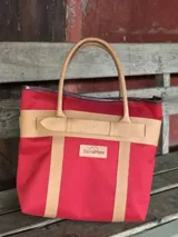 Bolso de playa de lona color verde claro con detalles en cuero color beige. Tiene doble asa de hombro y cierre superior con tira de cuero.