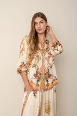 Blusa color crema con estampado floral y detalles de diseño barroco, con cuello mao, mangas 3/4 y cierre frontal con botones.