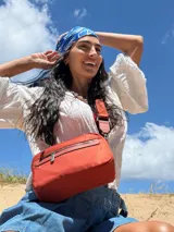 Bandolera color rosa viejo con detalles en cuero marrón claro, múltiples cremalleras metálicas y herrajes plateados. Incluye correa ancha ajustable con el logo de la marca.