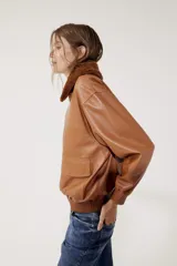 Campera bomber de cuero color marrón con cierre frontal, cuello clásico, bolsillos plaqué con tapa y puños y cintura acanalados.