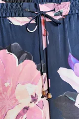 Pantalón de tiro alto con estampado de flores rosas y lilas sobre fondo azul marino. Tiene bolsillos delanteros y falsos bolsillos traseros. La cintura es elástica y ajustable con cordones.