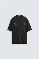 Camiseta negra de corte relaxed fit, cuello redondo y manga corta. Presenta estampaciones combinadas a contraste en el delantero y la espalda.
