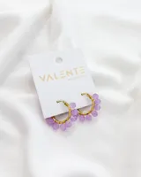 Aros de acero dorados con forma de argolla, decorados con pequeñas cuentas de color lila.