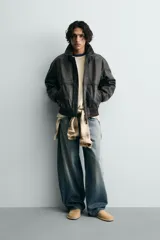 Cazadora bomber de piel color marrón oscuro envejecido, con cuello solapa, cierre frontal de cremallera y puños y bajo en rib elástico. Presenta grabados en relieve en el delantero y la espalda.