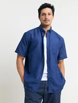 Camisa de manga corta azul con pequeños lunares blancos, cuello abotonado y bolsillo en el pecho.