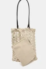 Bolso tipo shopper de tamaño pequeño, tejido en crochet color beige claro con patrón calado. Incluye asas de hombro de cuero sintético marrón oscuro y una bolsa interior con cierre de cremallera.