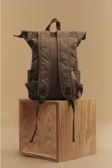 Mochila marrón de lona con detalles en cuero, cierre superior enrollable con hebillas y dos bolsillos frontales con hebilla.