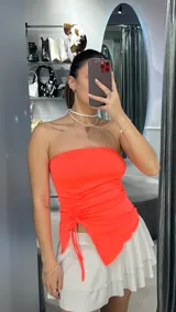 Top strapless color fucsia neón con frunces laterales y corte irregular en el ruedo.