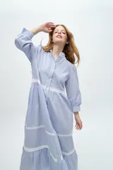 Vestido camisero midi color beige a rayas verticales, con cuello mao, mangas 3/4 abullonadas y festones de algodón en el cuerpo. Cierre frontal con botones.