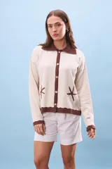 Cárdigan color crema con cuello y borde inferior marrón. Tiene cierre frontal con botones y bordados de estrellas de mar.