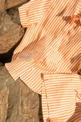 Camisa de lino a rayas verticales color naranja y blanco, de manga corta y corte oversize. Presenta bordados con motivos playeros en el frente y la espalda.