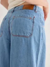 Pantalón gris de tiro medio alto, corte ancho, con bolsillos delanteros y traseros, detalles de atraques y triples costuras en color amarillo.