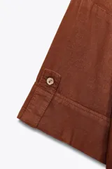 Camisa de lino color celeste claro, con cuello solapa, escote pico, manga corta con vuelta y dos bolsillos de plastrón en el delantero. Cierre frontal con botones.