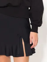 Minifalda negra confeccionada en lycra doble, con cierre lateral y tiracierre en tela base. Tiene doble capa de volados caracol en el ruedo y tajo con moño en tela complemento.