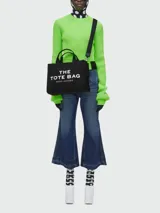 Bolso tote mediano color beige con estampado frontal del logo "The Tote Bag Marc Jacobs" en blanco. Tiene doble asa corta y correa larga extraíble de tela azul marino.