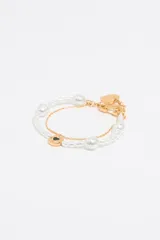 Pulsera doble con una hilera de perlas y otra de cadena dorada. Incluye un dije redondo con un corazón esmaltado y un dije de corazón liso.