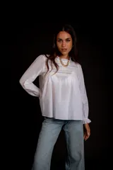 Camisa color crema con cuello alto y mangas largas con volados en los puños. Presenta detalles de crochet y broderie en el frente.