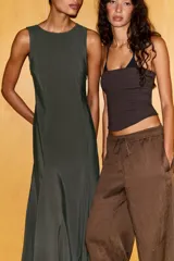 Vestido midi color verde oscuro, confeccionado en tejido fluido. Presenta cuello redondo, manga sisa y bajo con línea evasé y pliegues. Tiene cierre lateral con cremallera oculta y cierre en la espalda con abertura y botón.