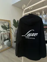 Buzo hoodie negro de corte oversize, con capucha, bolsillo frontal y estampa blanca en la espalda con la leyenda "Luxe" y "The Luxe Vip Club".