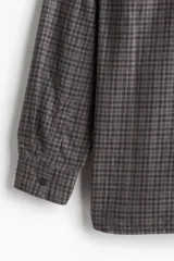 Camisa de franela suave a cuadros grises y marrones, de corte holgado, con cuello inglés, tapeta clásica, canesú en la espalda, bolsillo superior abierto, mangas largas con tapeta de manga y puños abotonados, y bajo levemente redondeado.