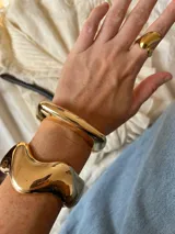 Brazalete rígido dorado con forma cuadrada y cierre a presión.