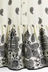 Vestido corto de viscosa color crema con estampado paisley en negro, cuello mao, botones frontales, mangas largas abullonadas con puños abotonados y falda con volantes.