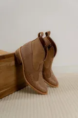 Botines de cuero marrón y blanco con diseño western, puntera redondeada y cierre lateral con cremallera. El talón tiene una tira de cuero para facilitar el calce.