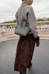 Bolso mini shopper de cuero sintético color gris oscuro, con doble asa de mano y detalles de ojales metálicos en los laterales. Incluye asa extraíble para llevar como bandolera y cierre magnético.