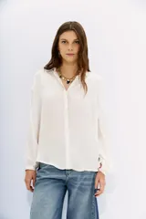 Camisa blanca de manga larga confeccionada en viscosa con acabado sandwash, de textura suave y aterciopelada. Cuello camisero con botón en forma de corazón y frunces en el canesú delantero y la espalda.