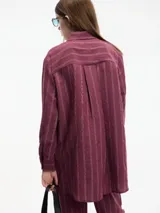 Conjunto de camisa y pantalón a rayas verticales color borgoña. La camisa es de manga larga con cuello camisero y botones frontales. El pantalón es de corte recto con cintura elástica y cordón ajustable.