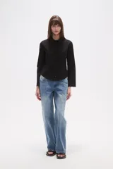 Camisa blanca de algodón, entallada, con cuello camisa y cierre frontal de botones. Presenta mangas largas con puños sencillos.