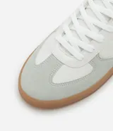Championes urbanos de corte bajo, color blanco con detalles en gris y negro. Confeccionados en material sintético con recortes efecto gamuza y suela de látex color caramelo.