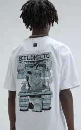Remera blanca de algodón premium con estampa gráfica grande en la espalda. La estampa presenta un personaje encapuchado leyendo un libro sobre barriles, con el texto "KILOMBITO" en la parte superior y una lápida con el texto "QUE NO ENTIENDAN NADA" en la parte inferior. Presenta un pequeño logo de tijeras bordado en la nuca.