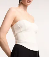 Blusa tipo corset color crema, sin breteles, confeccionada en crepé con bajo asimétrico alargado.