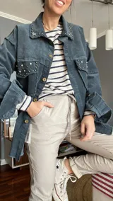 Camisa de pana azul con cuello clásico, cierre frontal con botones dorados, bolsillos con solapa y detalles de strass en cuello y bolsillos. Mangas largas con puños abotonados.