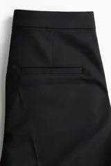 Pantalón cigarette tobillero negro con cintura estándar, cierre y pretina prolongada con corchete oculto. Piernas ajustadas con abertura corta en los bajos, bolsillos al bies y bolsillo de atrás decorativo. Pliegues adelante y atrás.